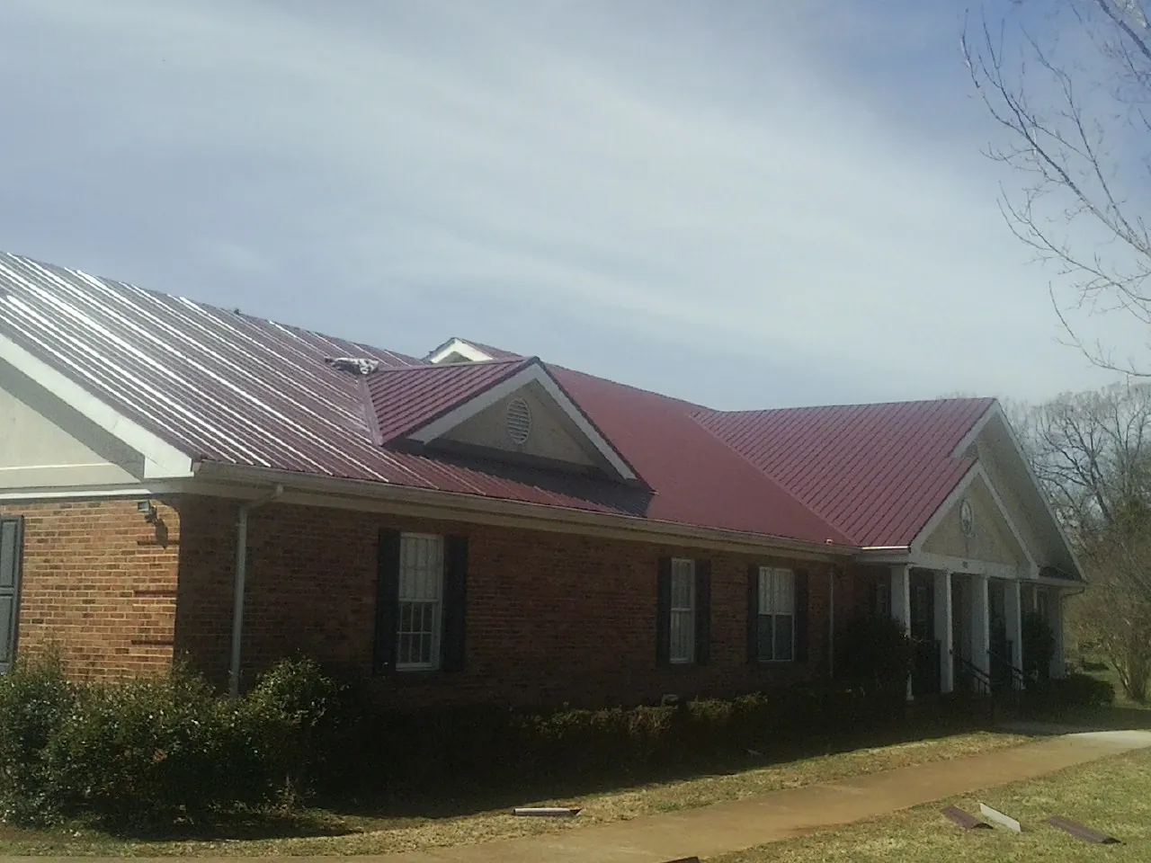 Red metal roof with gabled entries on a long brick building, from a Hail Damage Roof Repair job in Aredale