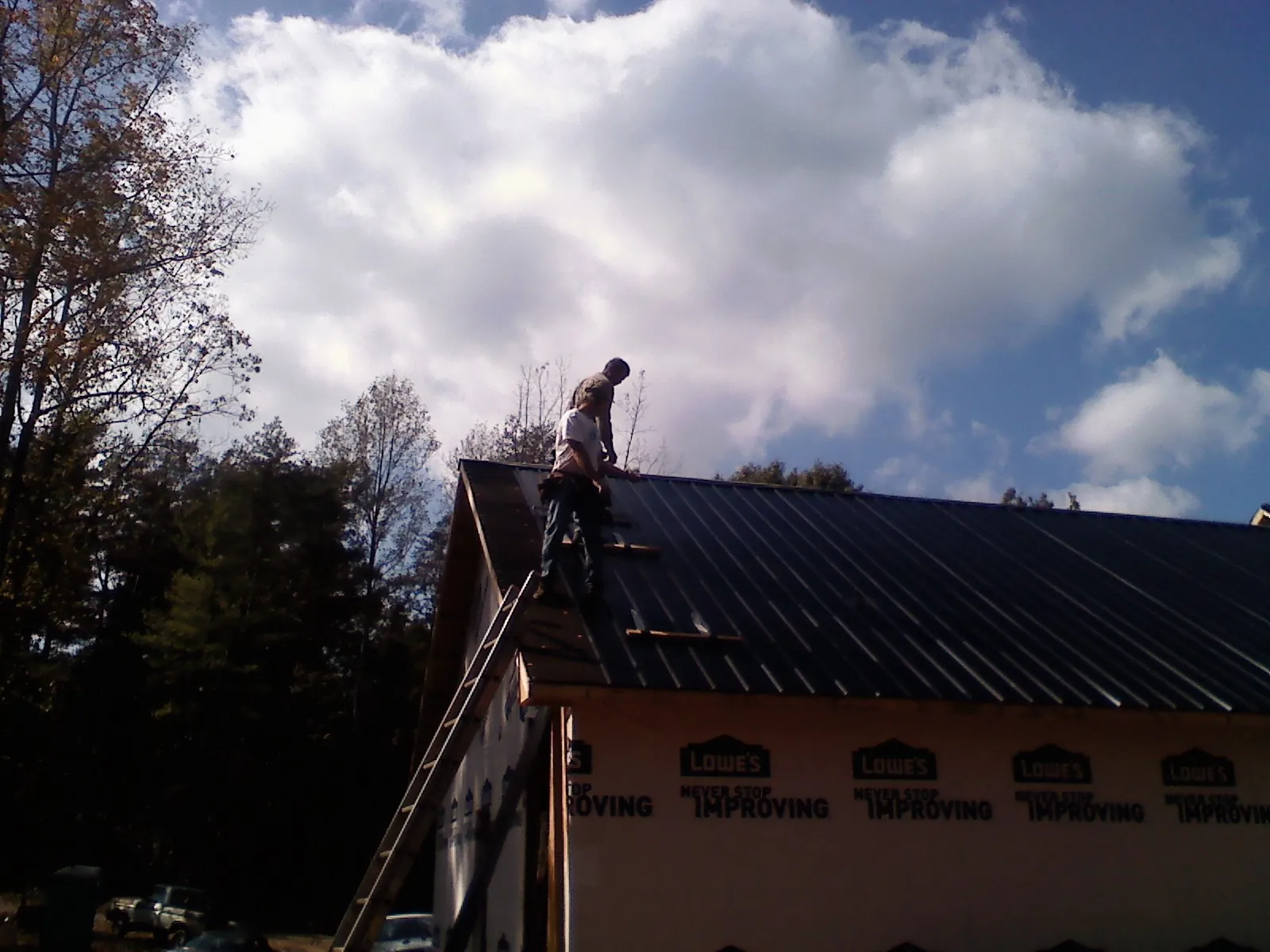 Roofer fastening dark metal panels high against a cloudy sky, from a Roof Inspection job in Aredale