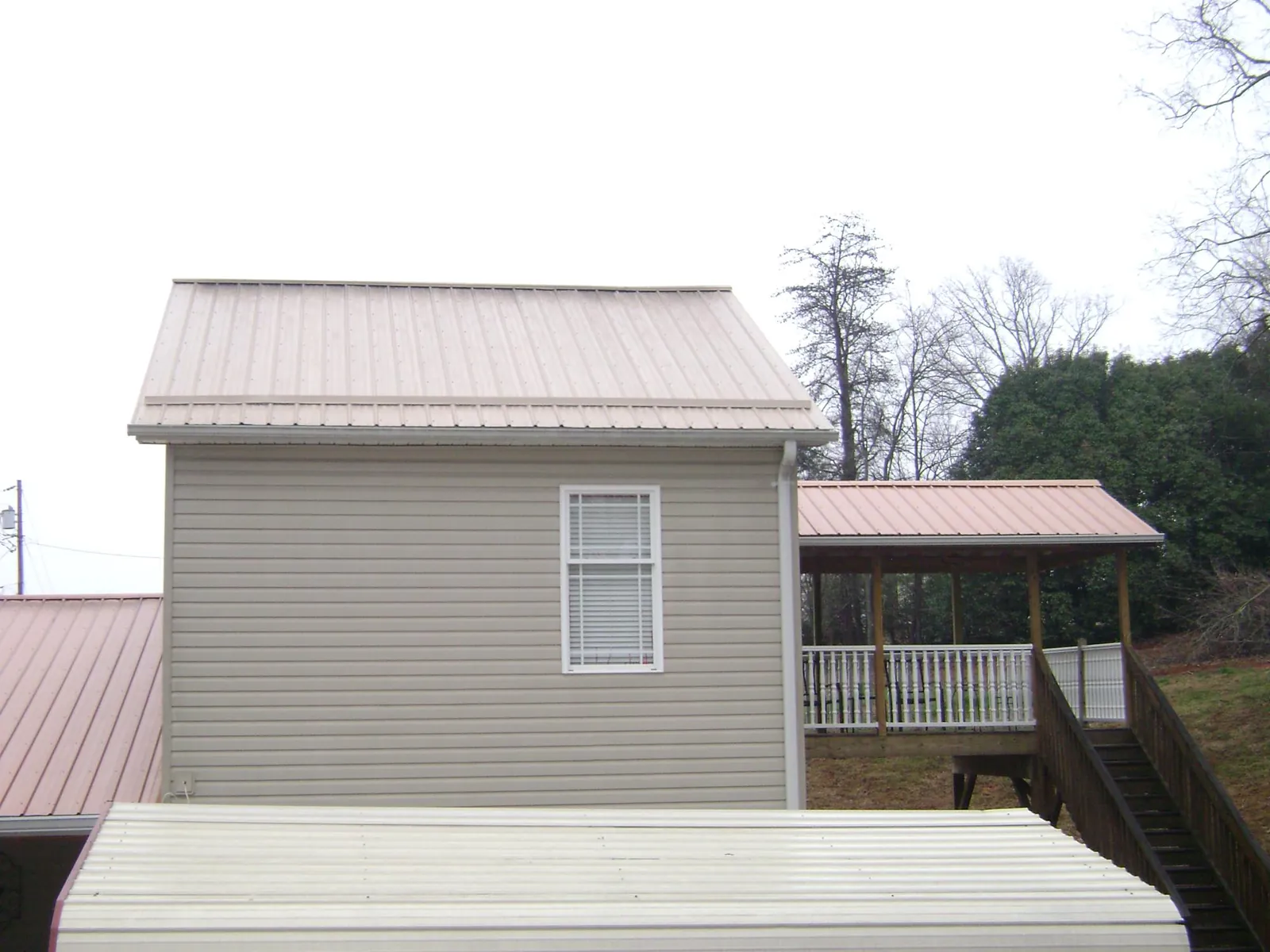 Tan metal roofs on a two story addition and attached porch, from a Roof Replacement job in Aredale